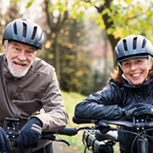 Ouder stel kijkt lachend en staat met de fiets in de hand en helmen op.