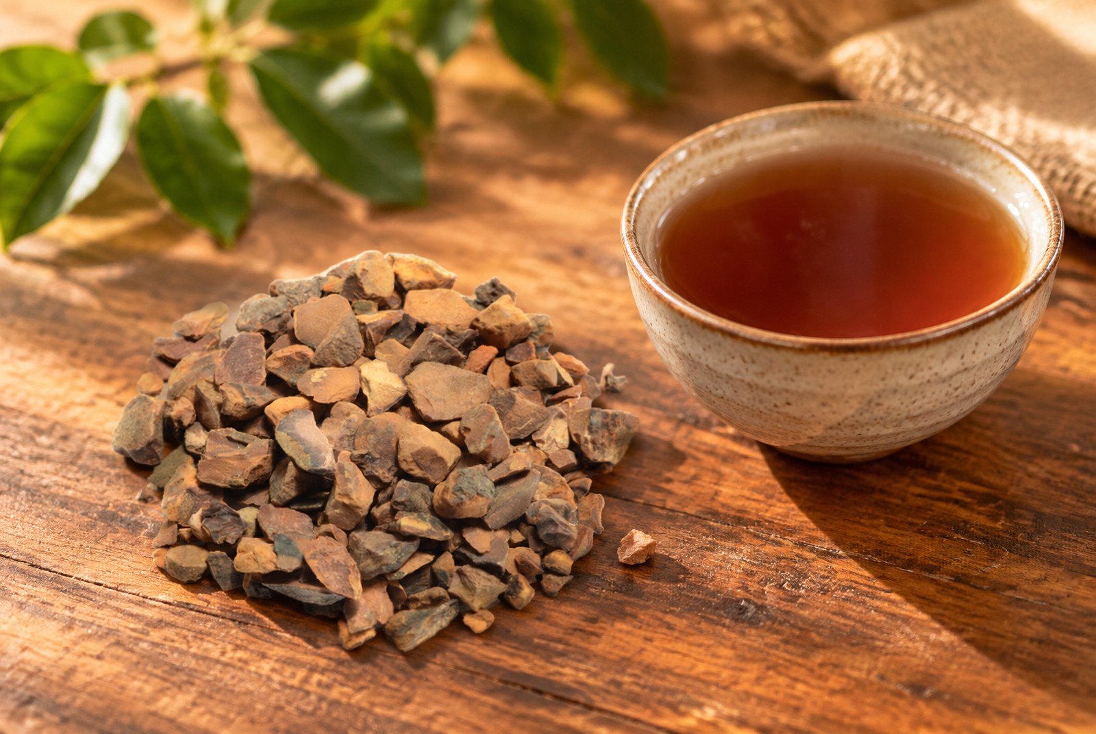 Dried kola nut pieces next to a bowl of kola nut tea on a wooden table