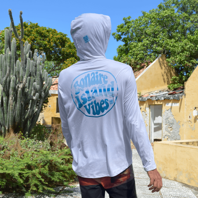 Model draagt een parelwitte UV-hoodie met 'Bonaire Island Vibes' design verwerkt in een drone shot van Kenny Ranking op Sorob