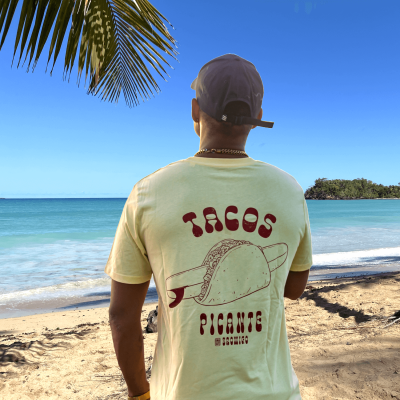 Model kijkt uit over de Caribische zee met een geel T-shirt met rugprint van een surfboard in een Mexicaanse taco