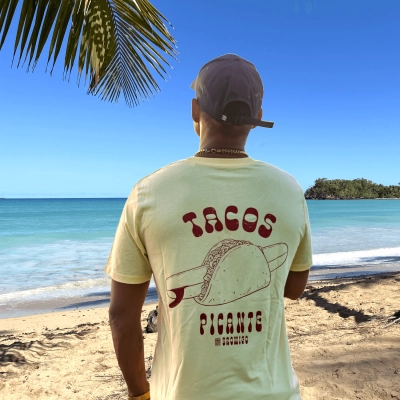 Model kijkt uit over de Caribische zee met een geel T-shirt met rugprint van een surfboard in een Mexicaanse taco