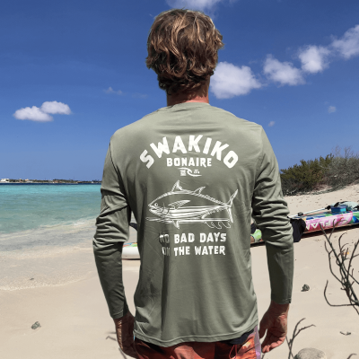 Model draagt op het strand een Olijf groen Swakiko surf shirt, rashguard, met print van een tonijn op een surfboard en de tek