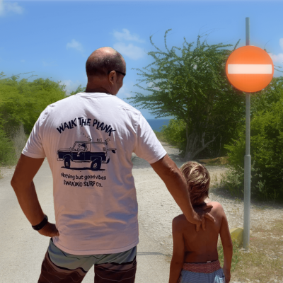 André draagt een wit 'Walk the plank" T-shirt met een chille surfer in zijn jeep met surfboards en vogeltjes op het dak.