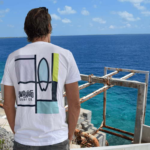 Model kijkt uit over zee en draagt een wit Swakiko t-shirt met een design in de stijl van Mondriaan 