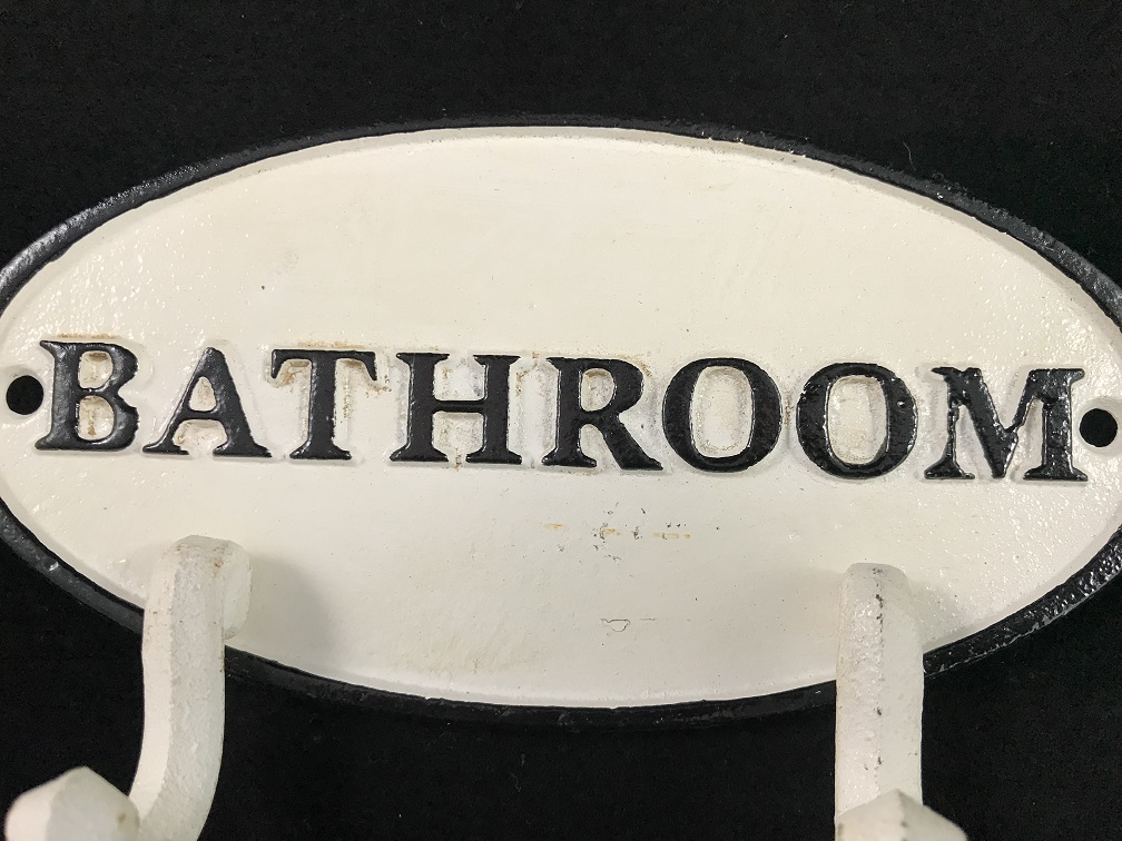 Een kapstok met 2 haken, bord met opschrift: 'BATHROOM' als achtergrond, gietijzer