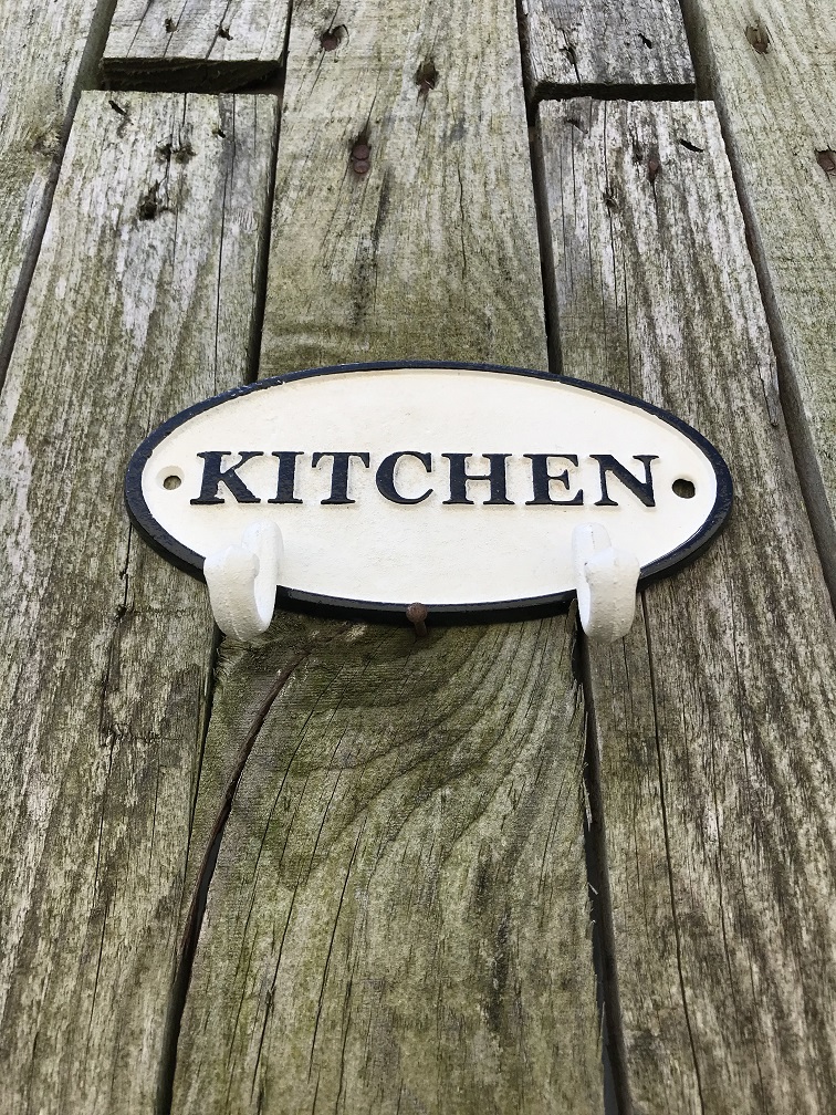 Een kapstok met 2 haken, bord met opschrift: 'KITCHEN' als achtergrond, gietijzer