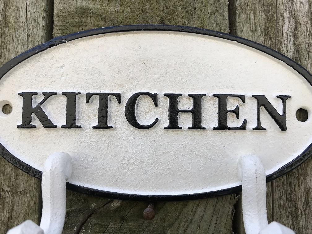 Een kapstok met 2 haken, bord met opschrift: 'KITCHEN' als achtergrond, gietijzer
